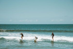 pexels-photo-4603608-4603608 Three people surfing on ocean waves with clear blue sky, capturing outdoor adventure.